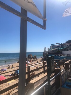 A beach with a wooden walkway, umbrellas, and a building with a sign.