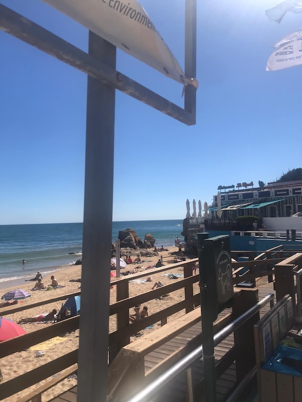 Una playa con un paseo de madera, sombrillas y un edificio con un letrero.