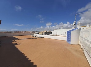 Una terraza en la azotea con vistas despejadas del paisaje urbano, un edificio blanco con detalles azules y una antena parabólica.