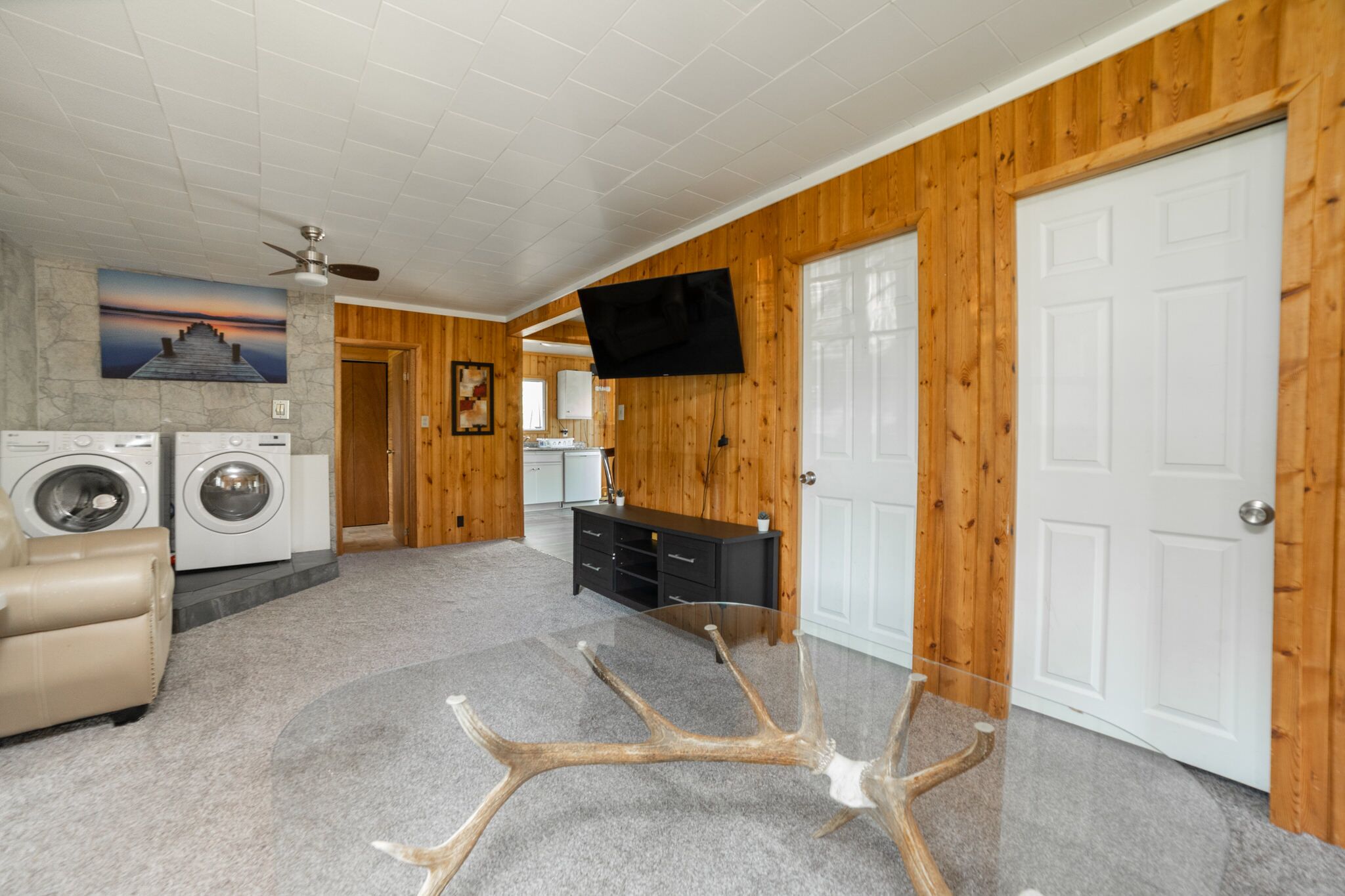 Ein Waschraum mit Waschmaschine und Trockner, einem Deckenventilator und einem an der Wand befestigten Fernseher.
