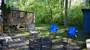 A deck with a chair and a fire pit in a wooded area.