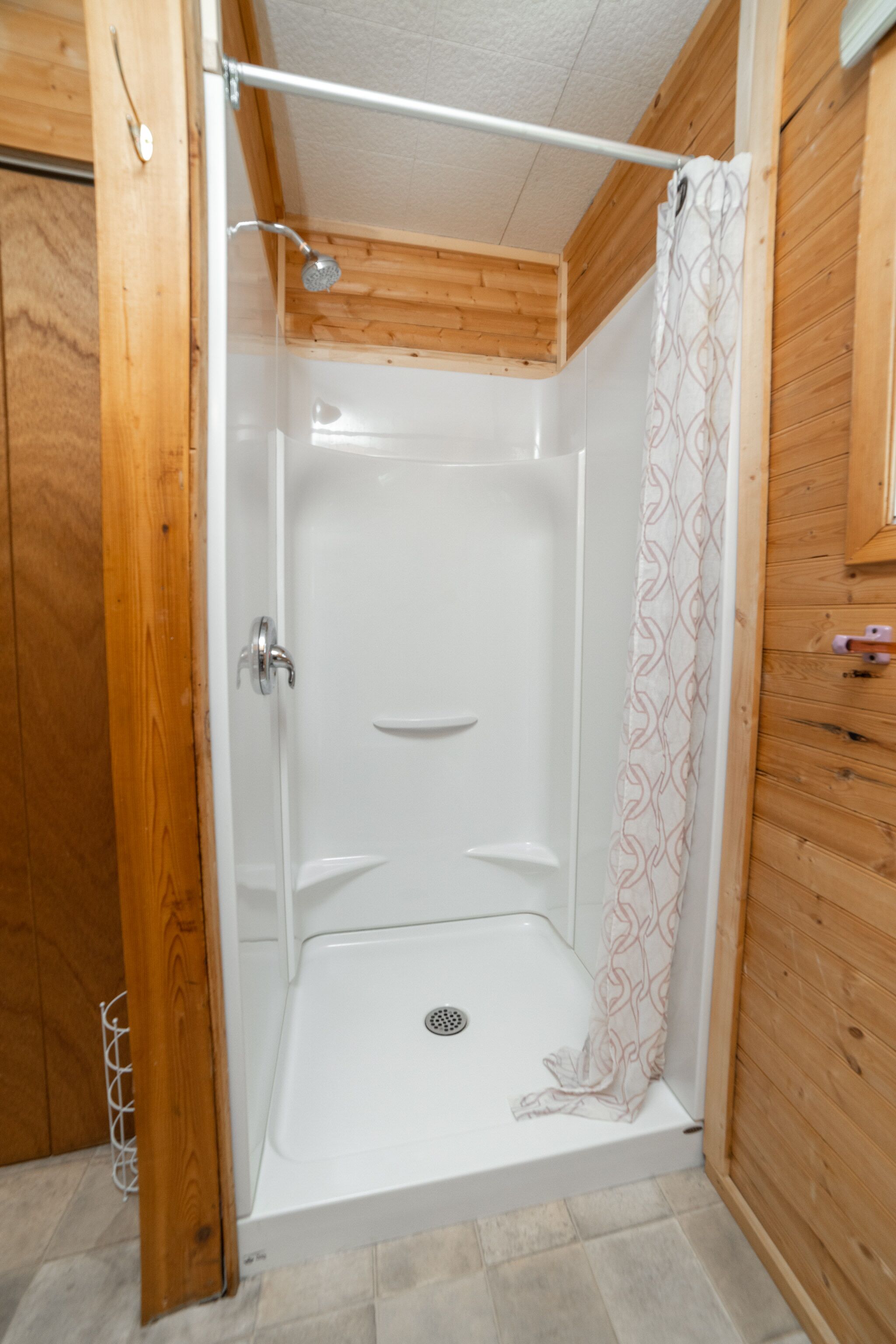 A shower stall with a white door, a showerhead, and a patterned shower curtain.
