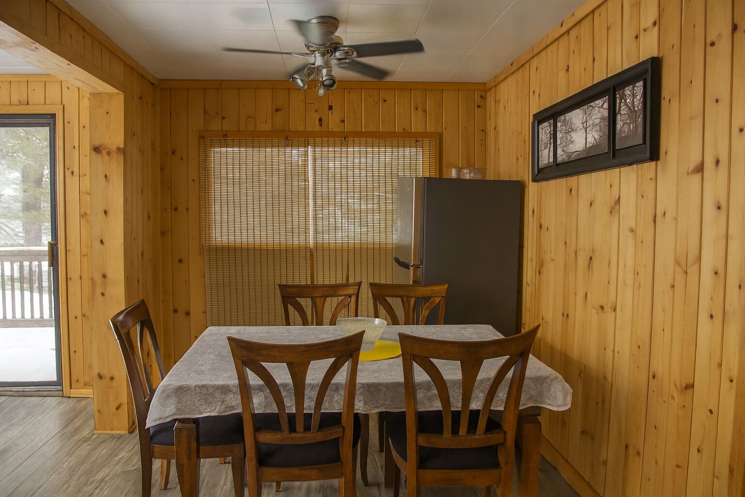 A dining area with a table, chairs, a ceiling fan, a refrigerator, and a window with blinds.