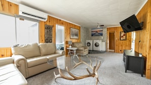 Una sala de estar acogedora con una mesa de centro de vidrio, un sofá color beige y una pared de madera.