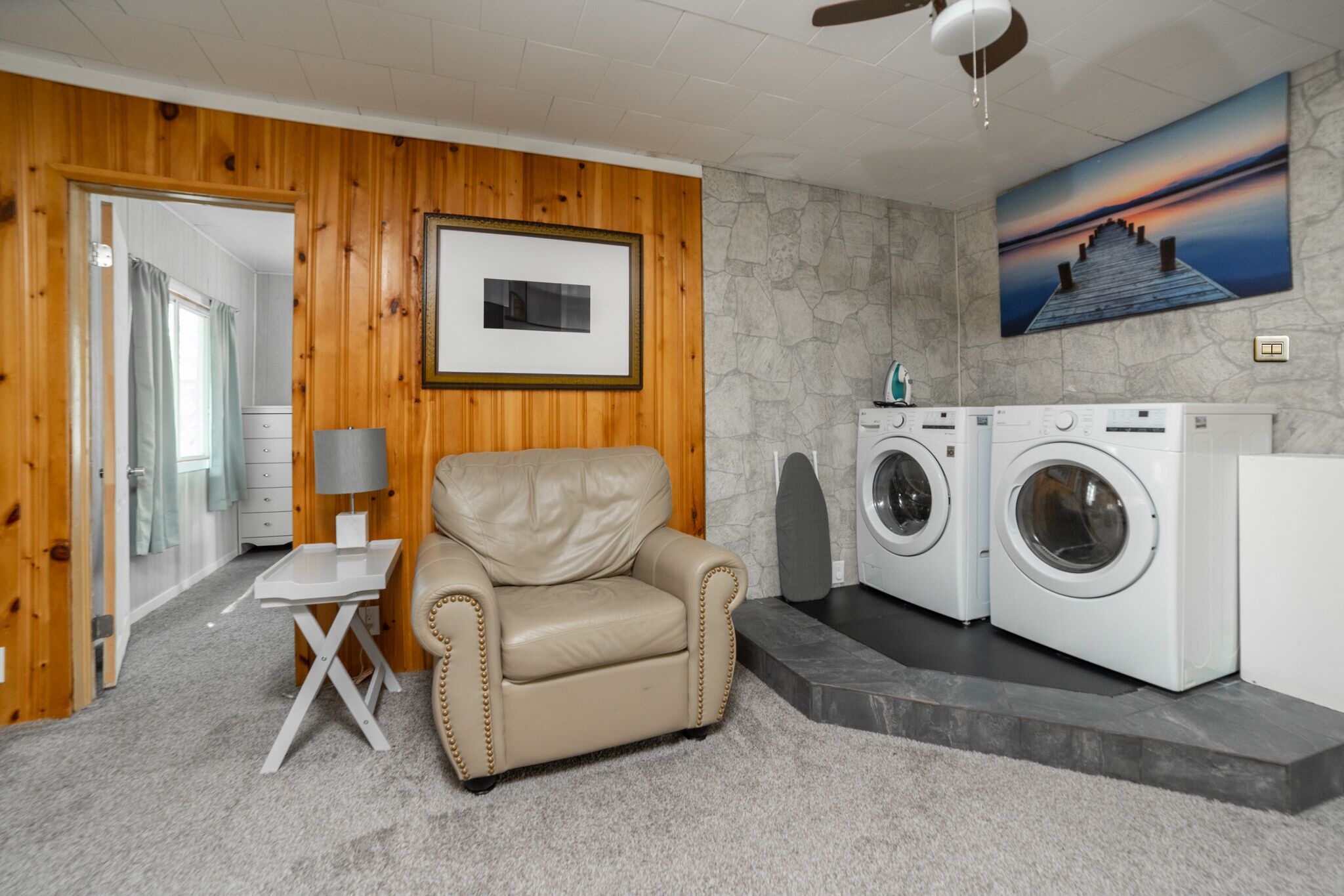 A laundry room with a beige leather chair, a small table, and two washing machines.