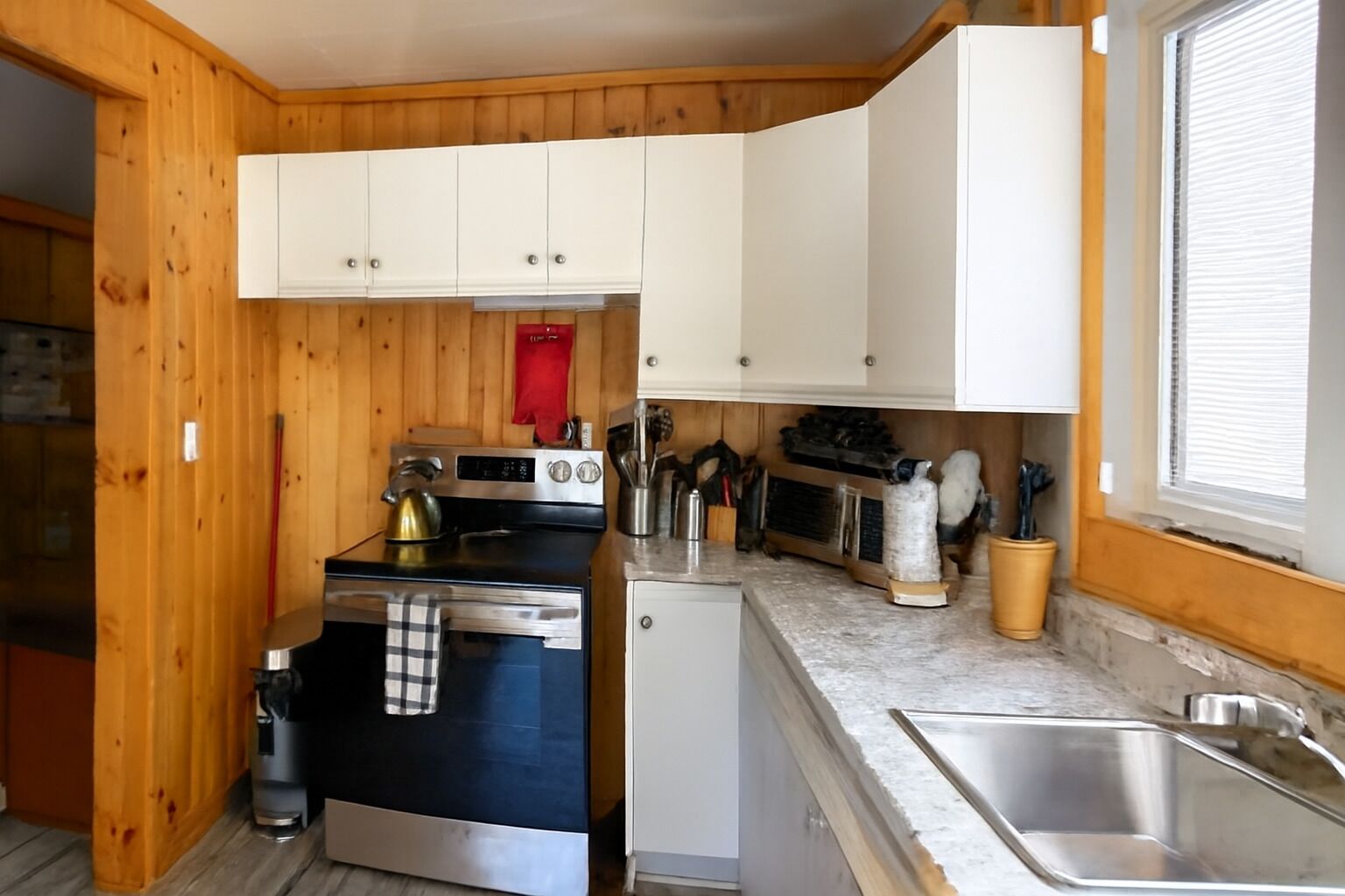 Una cucina compatta con pareti in legno, mobili bianchi, un fornello, un forno a microonde e un lavandino.