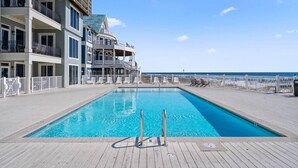 Ein Schwimmbad mit Holzterrasse, weißem Zaun und einem Gebäude mit Balkonen und überdachtem Bereich.