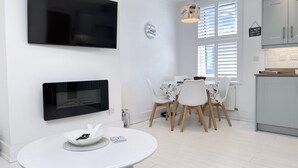 Una cucina moderna con mobili bianchi, un'area pranzo con un tavolo rotondo e sedie, un televisore a schermo piatto montato al muro e una lampada a sospensione sopra il tavolo da pranzo.