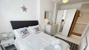 Un letto rifatto con lenzuola bianche e cuscini a righe, un comodino con una lampada, una cassettiera, uno specchio e una decorazione a stella sul muro.