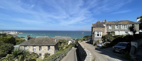 A coastal street with stone buildings, a paved road, and a view of the sea.