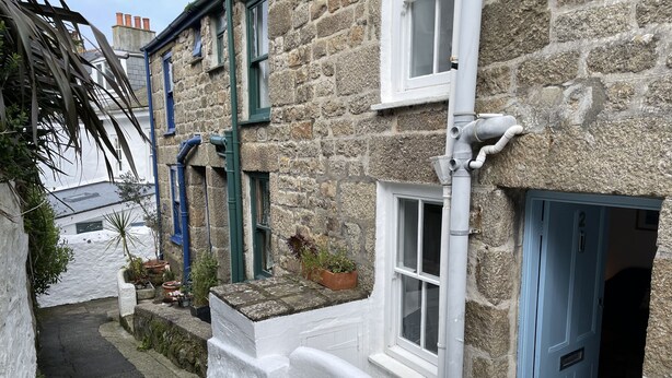 A narrow street with stone buildings, a white-painted exterior, and a blue door.
