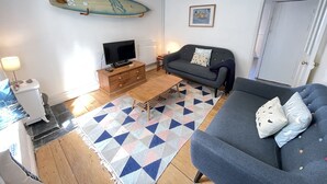 A living room with a sofa, a coffee table, a TV, a surfboard decoration, and a patterned rug.