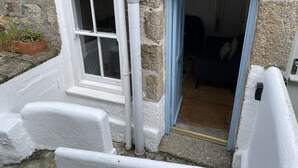A stone building with a white exterior, a window, and a door leading to an interior with a blue curtain.