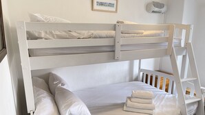 A bunk bed with white bedding and pillows, a framed picture on the wall, and a white air conditioner.