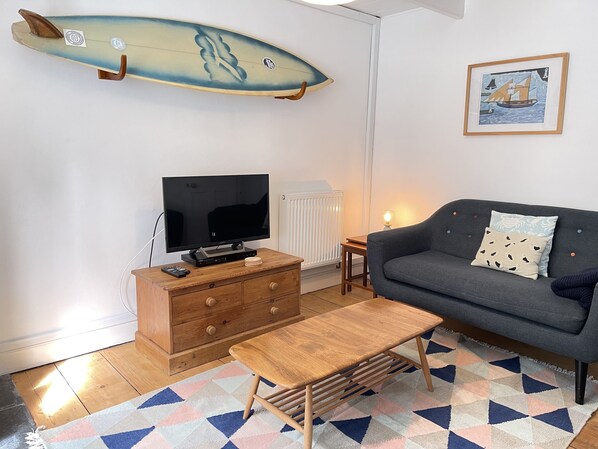 Ein Wohnzimmer mit Fernseher, einer Holzkommode, einem Sofa und einem an der Wand befestigten Surfbrett.