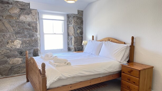 Ein Schlafzimmer mit Steinsandsteinwand, einem hölzernen Bett, einem Nachttisch und einem Fenster.