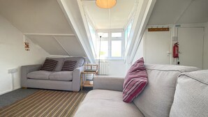 Ein modernes Schlafzimmer im Loft-Stil mit schrägem Dach, einem grauen Sofa, einem gemusterten Teppich und einer Hängeleuchte.