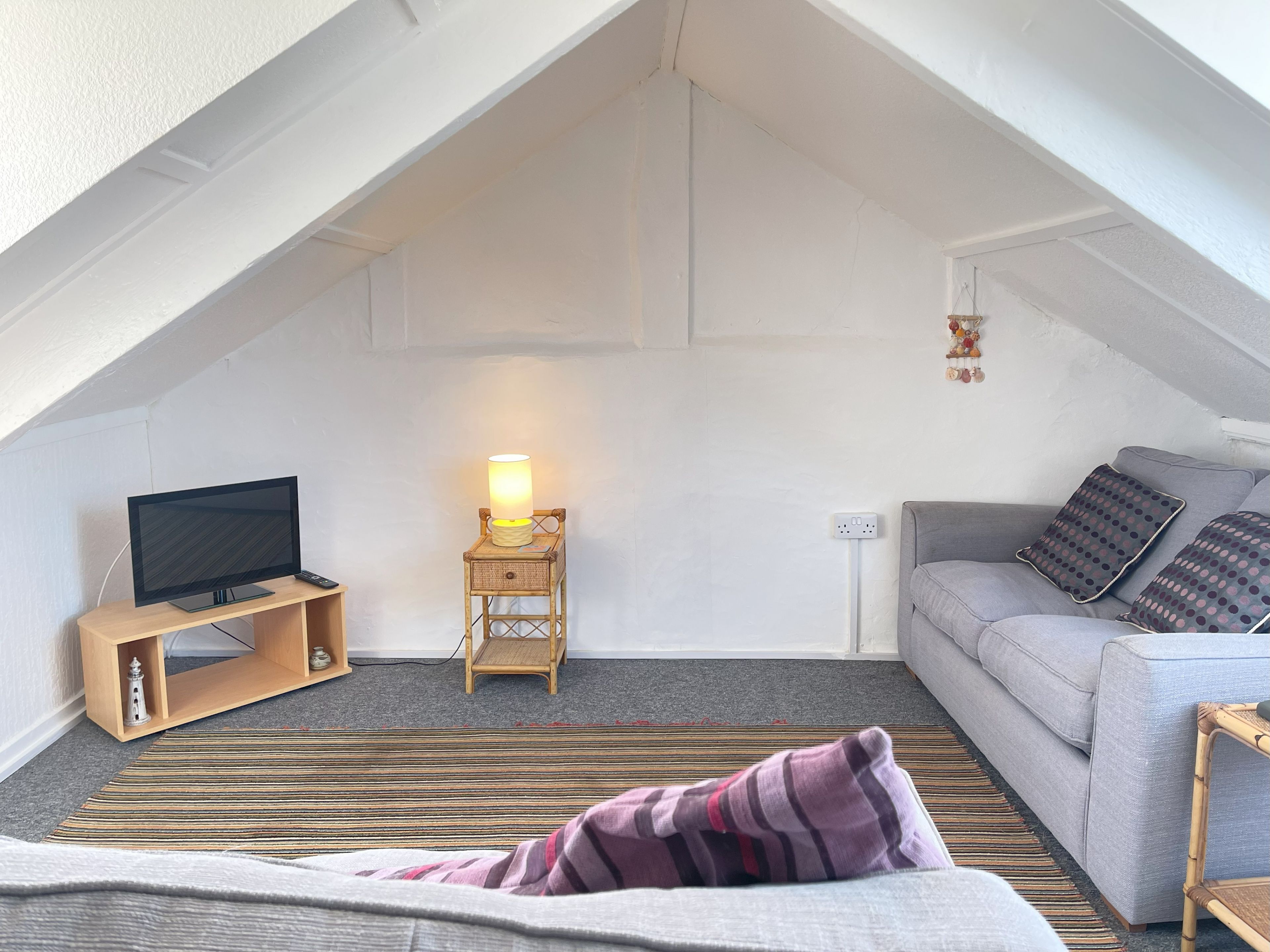A cozy attic room with a television, a lamp, a sofa, and a patterned rug.