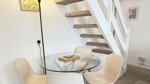 A modern room with a glass table surrounded by white chairs, a staircase with wooden steps, and a carpeted floor. - Lower Deck -  a cottage that sleeps 4 guests  in 2 bedrooms (St Ives)