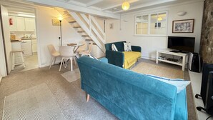 A living room with a sofa, TV, and a staircase leading to a kitchen. - Lower Deck -  a cottage that sleeps 4 guests  in 2 bedrooms (St Ives)