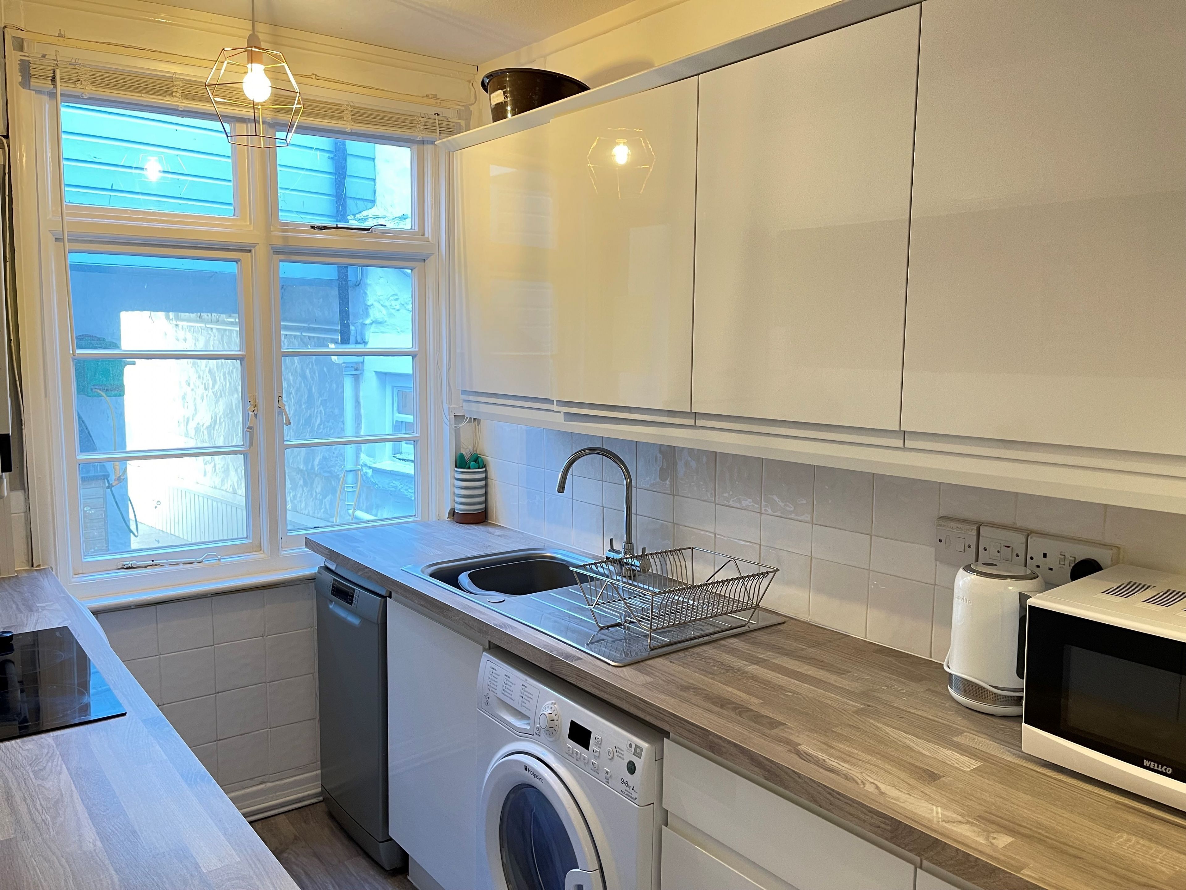 Une cuisine moderne équipée d’un lave-linge et d’un sèche-linge intégrés, d’un évier et d’un four à micro-ondes.