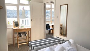 A hotel room with a bed, a desk with a chair, a radiator, and a window with a view of the city.