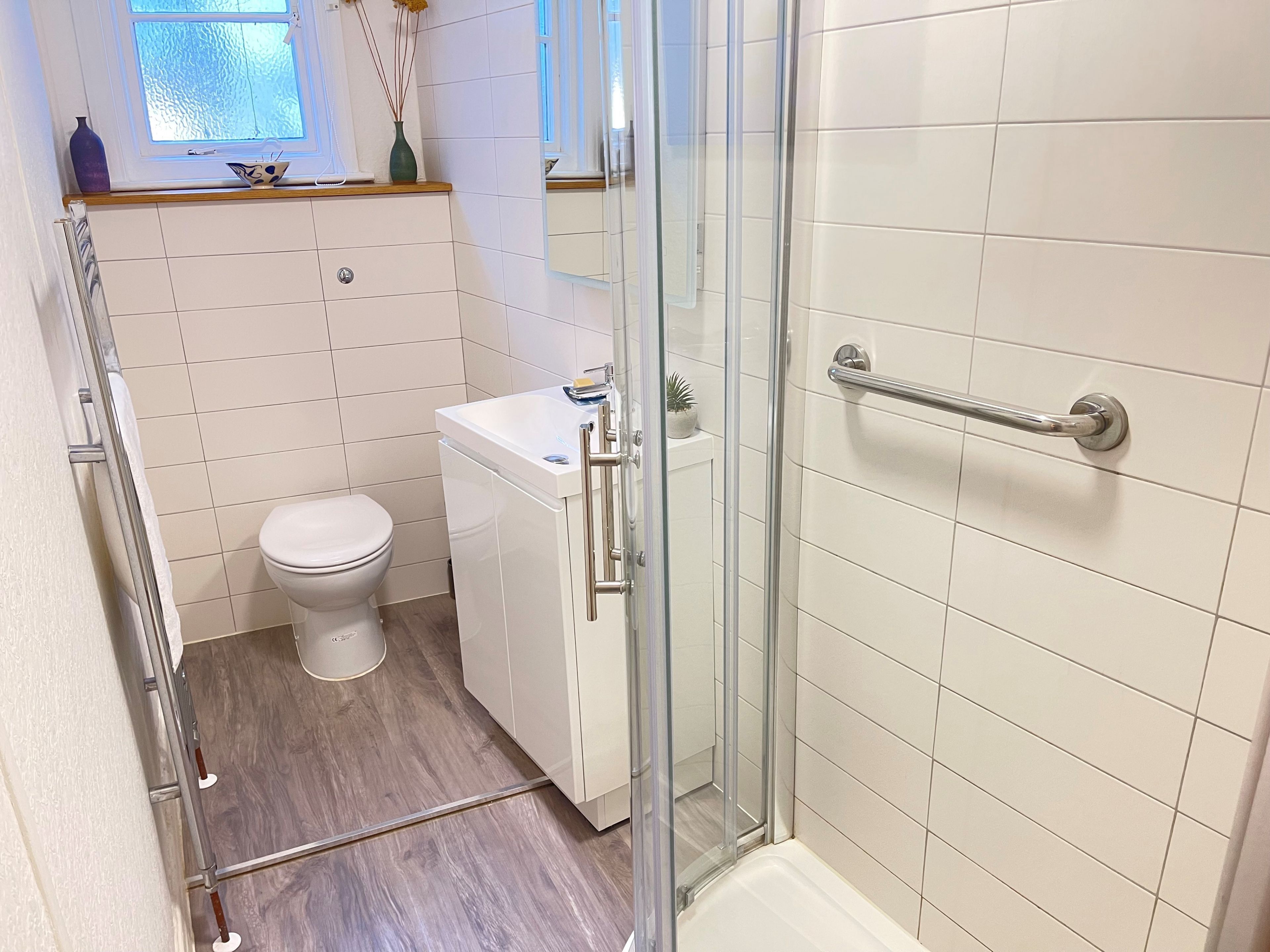 A bathroom with a toilet, a sink, a glass shower enclosure, and a wooden floor.