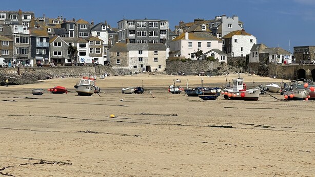 A beach with several boats anchored in the sand and a row of buildings in the background.