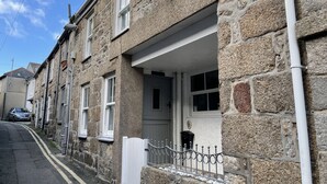 A stone-built residential building with a white front door, a small porch, and a metal fence. - The Bolt Hole - a cottage that sleeps 4 guests in 2 bedrooms (St Ives)