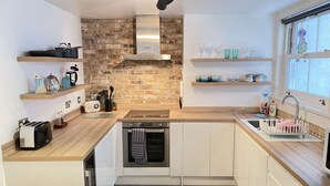 A modern kitchen with a brick wall, wooden countertops, a built-in oven, and a window with a view. - The Bolt Hole - a cottage that sleeps 4 guests in 2 bedrooms (St Ives)