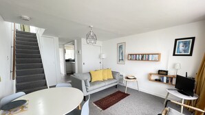 Un salon moderne avec un escalier, un coin repas et une cuisine en arrière-plan.