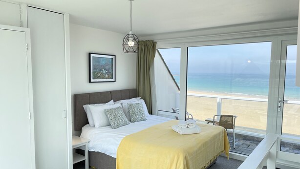 Une chambre d’hôtel avec un lit, une table de chevet, une chaise et un balcon offrant une vue sur la plage et l’océan.