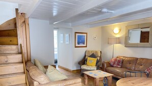 Uma sala de estar acolhedora com escada de madeira, sofás de couro, mesa de centro de madeira e mesa de jantar.