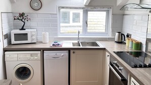 Uma cozinha compacta com máquina de lavar embutida, micro-ondas, pia e janela com vista.