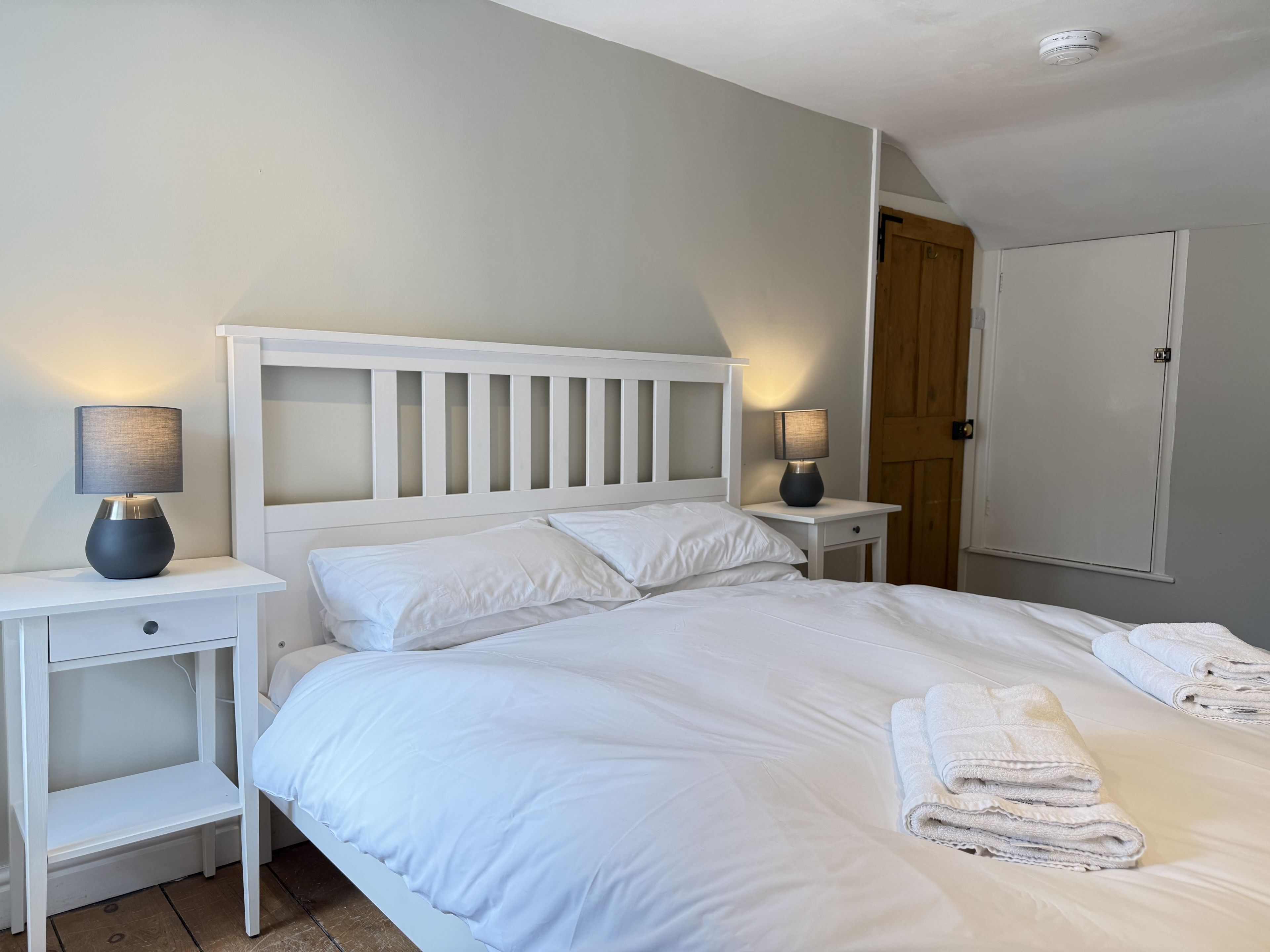 A neatly made bed with white linens and two bedside lamps.