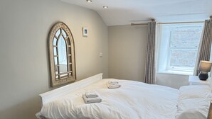 Quarto com cama grande, janela com cortinas, piso de madeira e espelho fixado na parede.