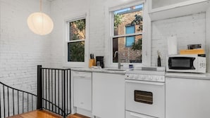 Une cuisine avec des meubles blancs, un four à micro-ondes, une cuisinière et un luminaire suspendu.