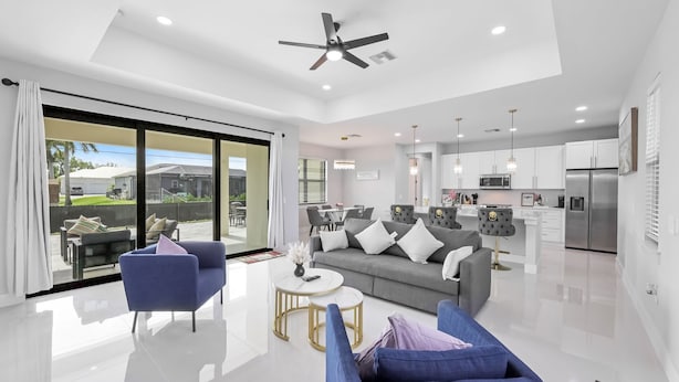 A modern living room with a sofa, chairs, and a coffee table. There is a kitchen area with cabinets and appliances in the background.