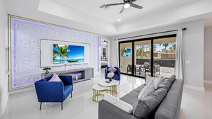 A modern living room with a flat-screen TV, blue and gray sofas, a coffee table, and a ceiling fan.