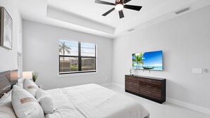 A bedroom with a bed, a TV, a ceiling fan, and a window with blinds.