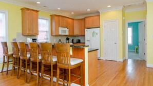 A kitchen with wooden cabinets, a microwave, a refrigerator, and a bar area with four stools. - Well equipped 5 bedroom home near Fort Fisher (Kure Beach)