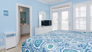 A bedroom with a large bed, a television, a dresser, and a bathroom visible through an open door. - Well equipped 5 bedroom home near Fort Fisher (Kure Beach)