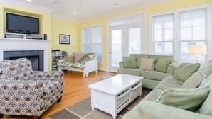 A living room with a fireplace, two sofas, a coffee table, and a television on a stand. - Well equipped 5 bedroom home near Fort Fisher (Kure Beach)
