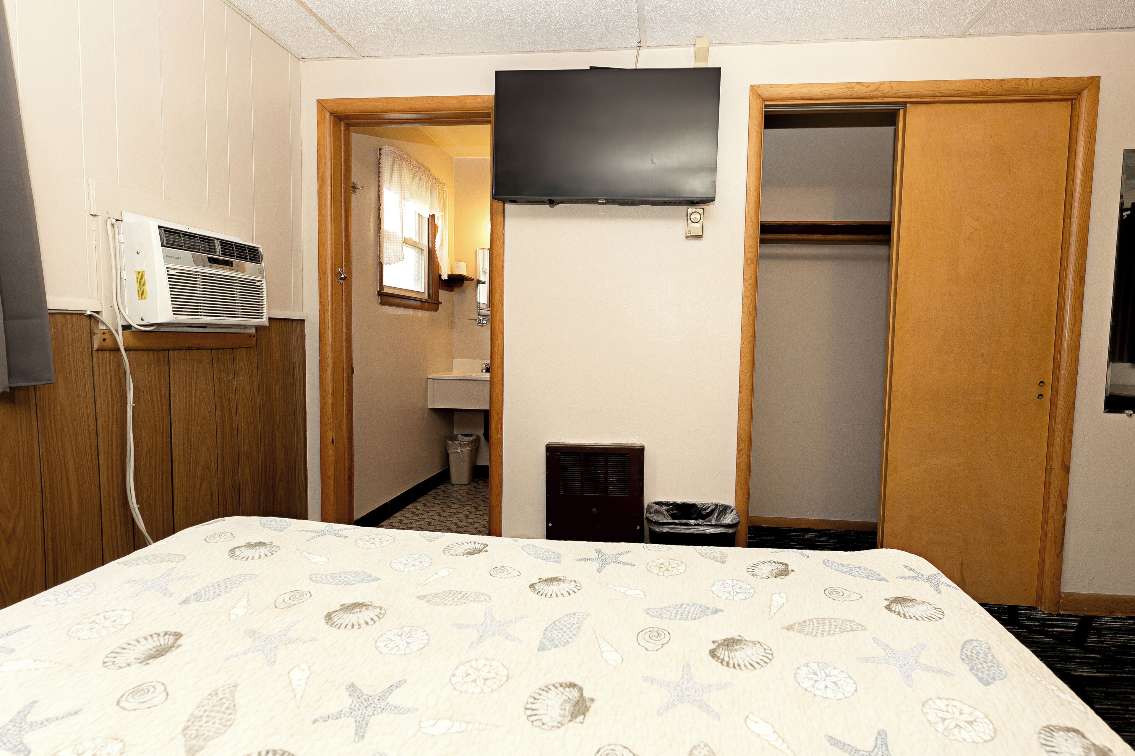 Ein Hotelzimmer mit einem Bett, einem an der Wand montierten Fernseher, einem Kleiderschrank und einer Klimaanlage.