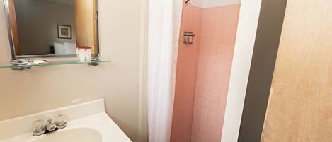 A bathroom with a sink, mirror, shower, and tiled walls.