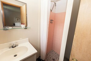 A bathroom with a sink, mirror, shower, and tiled walls.