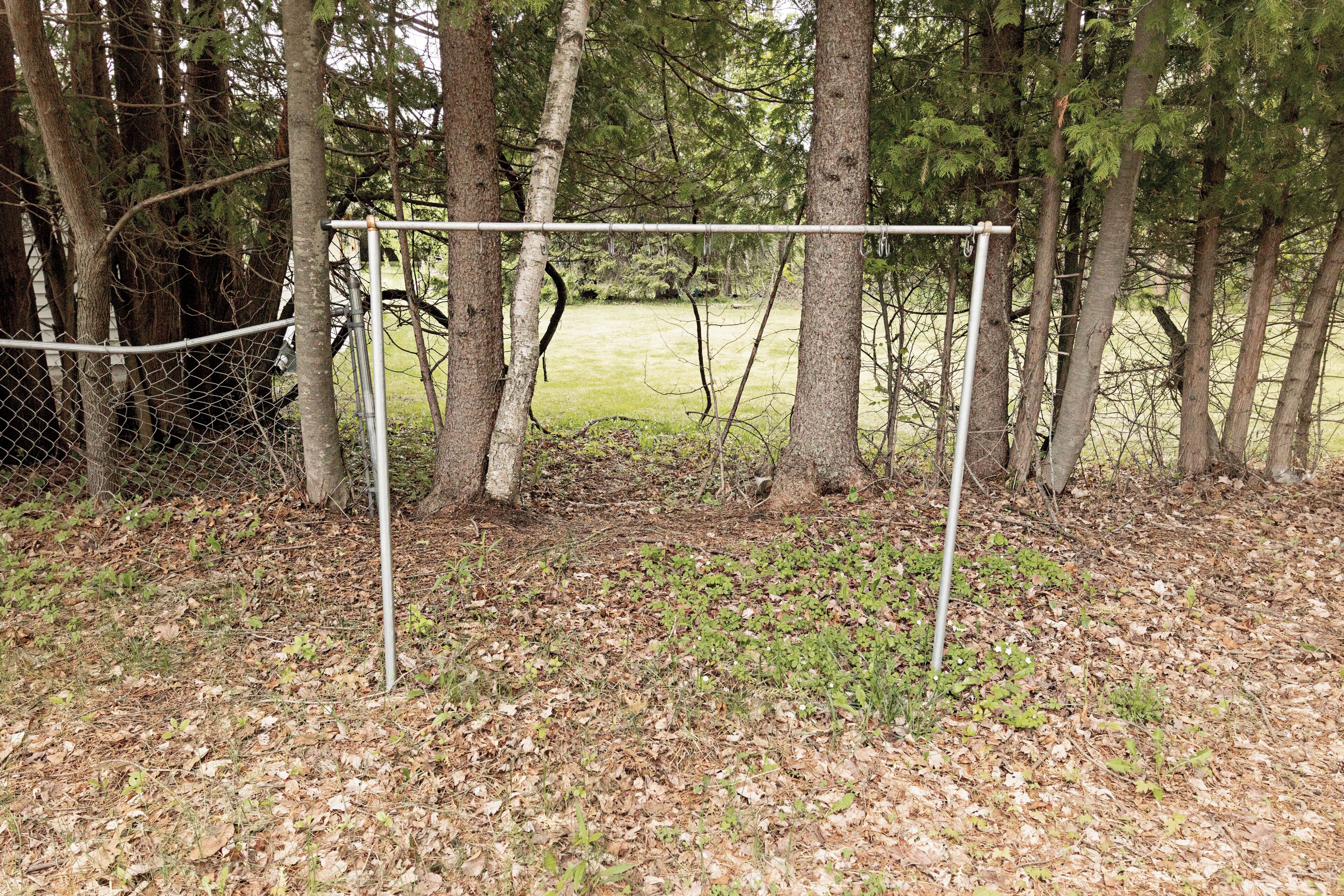 Un área cercada con un poste de portería, rodeada de árboles y un campo cubierto de césped.