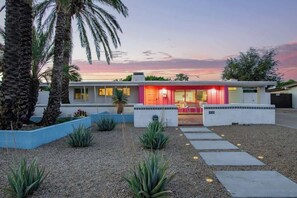 Una casa moderna con vialetto, palme e un tramonto.