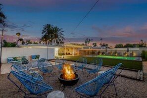 Un espace patio avec des chaises bleues, un foyer et une piscine en arrière-plan.