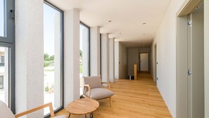 Um corredor moderno com grandes janelas, soalho de madeira e um espaço de estar com uma mesa redonda e cadeiras.